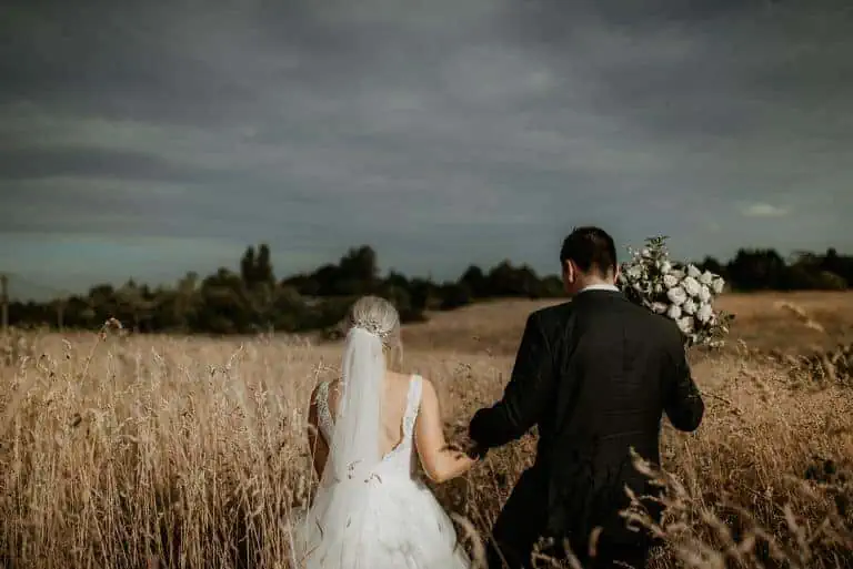 bride and groom walking in field of long grass