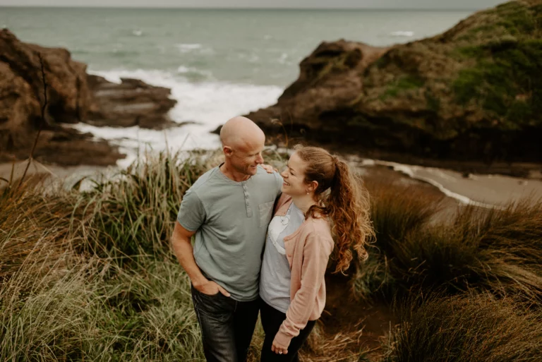 couple standing on cliff top at Piha Beach during an engagement shoot